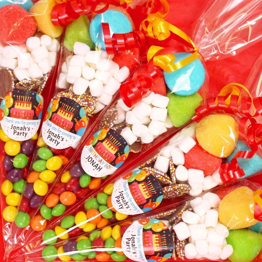 A close-up of pre-filled sweet cones with a variety of candies visible inside, decorated with colorful wrappers and personalized labels.