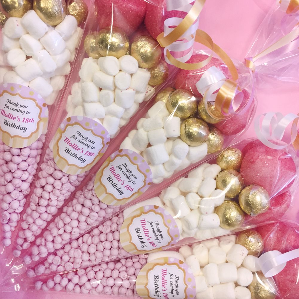 Assorted candy bouquet with pink, gold, and white candies in clear packaging, featuring personalised labels.
