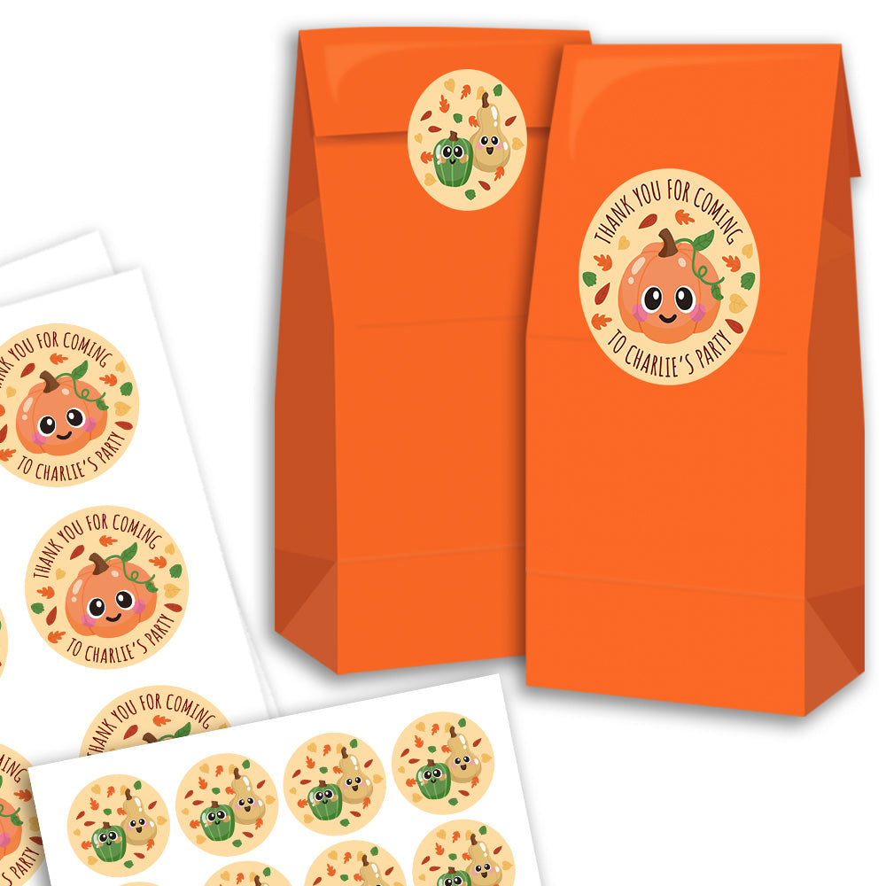Orange paper party favor bags with a round pumpkin-themed thank you sticker, shown alongside printed sheets of matching round stickers on a white background.