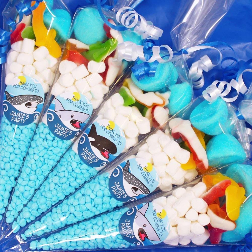 Packaged sweet cones with various colorful candies visible through the clear plastic wrapping. The packaging features shark graphics and text related to a birthday party.