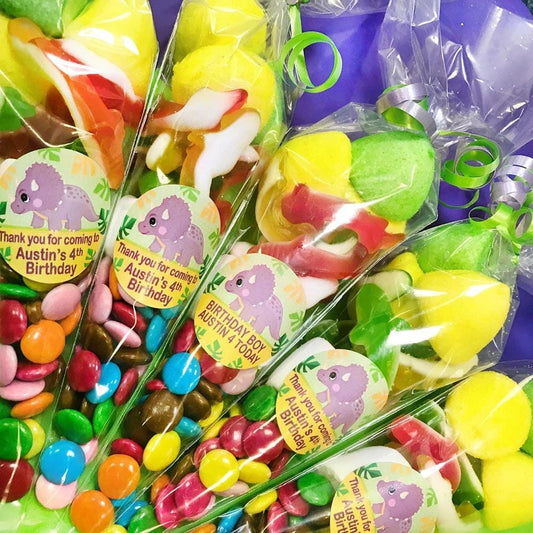 A close-up of a pre-filled sweet cone with various candies spilling out, decorated with a dinosaur sticker and labeled for a birthday party.