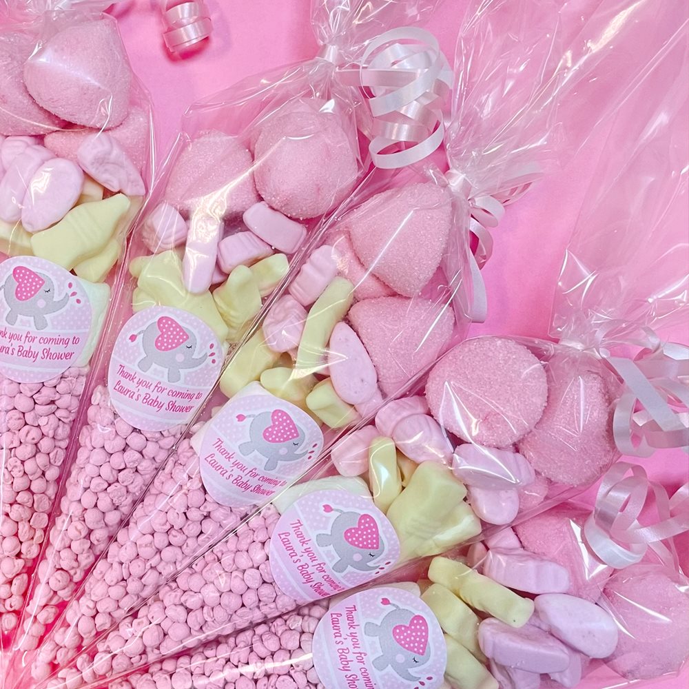 Pink and green candy bags with baby shower labels on a pink background