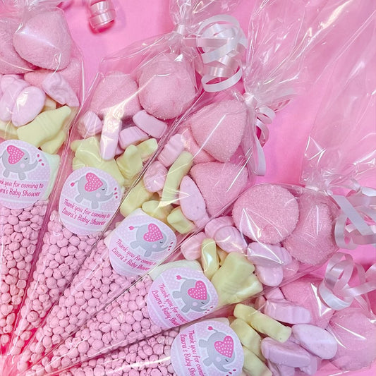 Pink and green candy bags with baby shower labels on a pink background