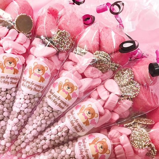 Pink candy cones with teddy bear labels for a baby shower on a pink background.