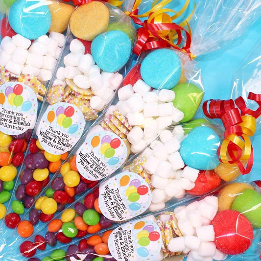 A selection of sweet cones with various candies and stickers, wrapped individually and tied with ribbons, intended as party favors.