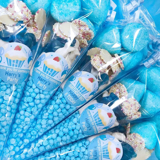 A collection of blue sweet cones with various candies visible at the top, each with a white sticker personalized for a party.