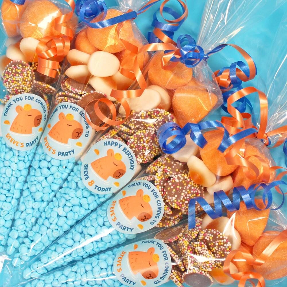 A collection of pre-filled sweet cones for kids' parties, with orange and white sweets visible, decorated with blue ribbons and personalised labels.