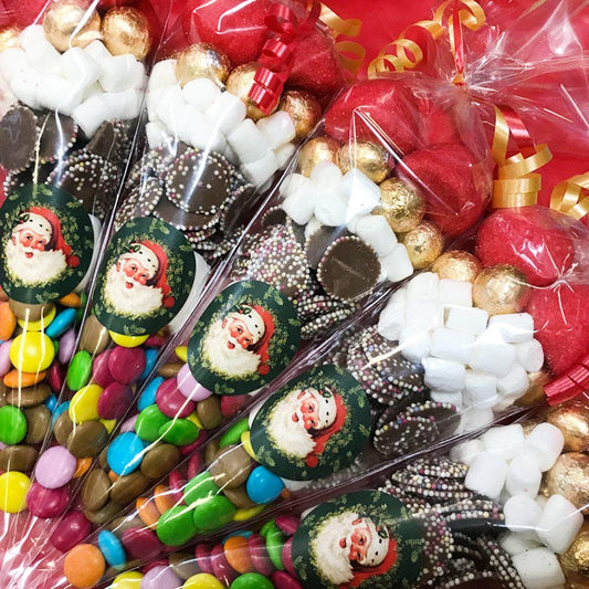 A selection of Christmas-themed sweet cones with various candies and chocolates visible, decorated with Santa faces and festive colors.