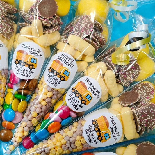A close-up of construction truck-themed sweet cones with various candies and stickers inside, sealed in plastic packaging with printed labels.