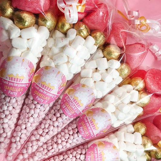 Assorted party favors including pink and gold candies with personalized labels.