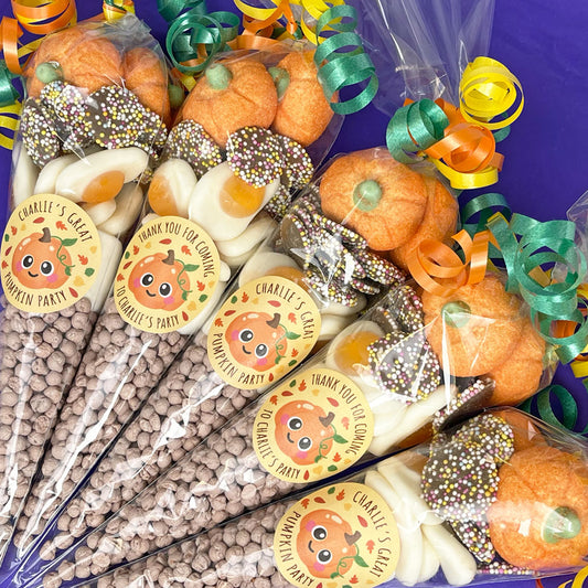 A set of fall-themed candy and snack gift bags arranged on a purple background. Each bag contains mini pumpkin-shaped candies, white chocolate pieces, sprinkles, and a clear cone filled with chocolate-coated chocolate chips.