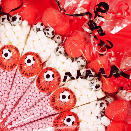 A close-up of a red football-themed sweet cone with various candies and decorations, including football-shaped sweets and personalized stickers with text.
