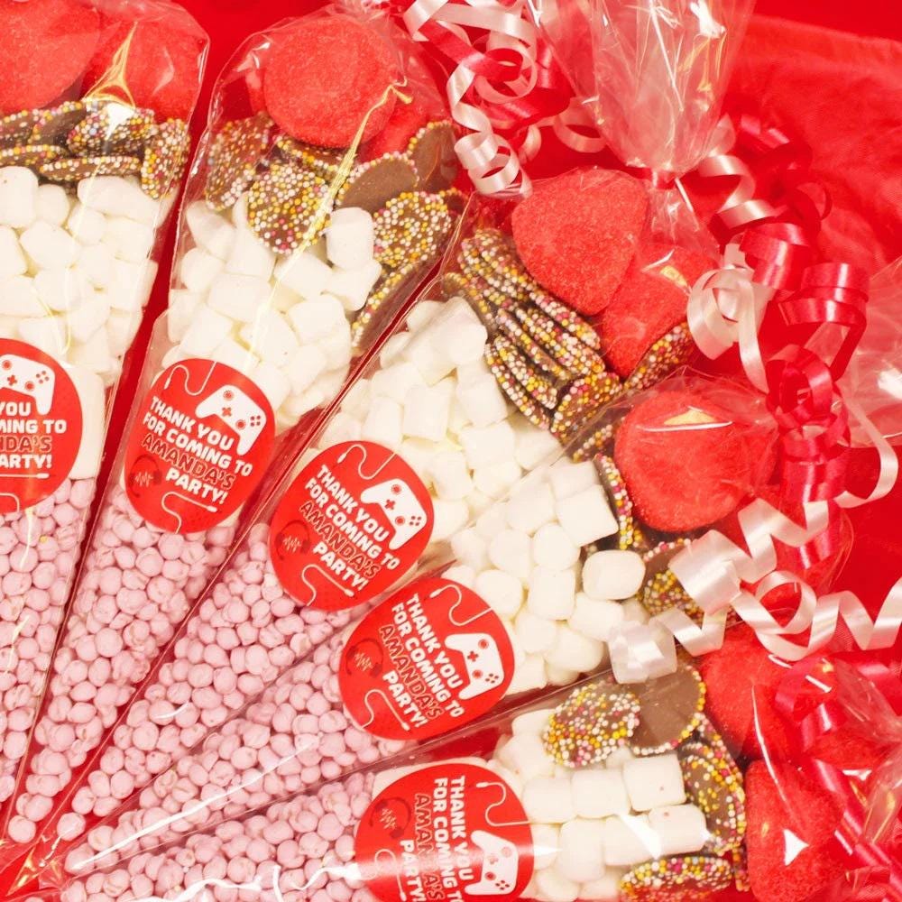 A red gaming sweet cone with various candies and toppings, wrapped with decorative ribbons and labels with messages.