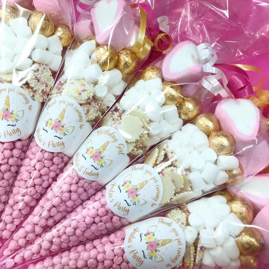 A collection of pre-filled sweet cones for children's parties, decorated with pink and white candy and branded with personalized labels.